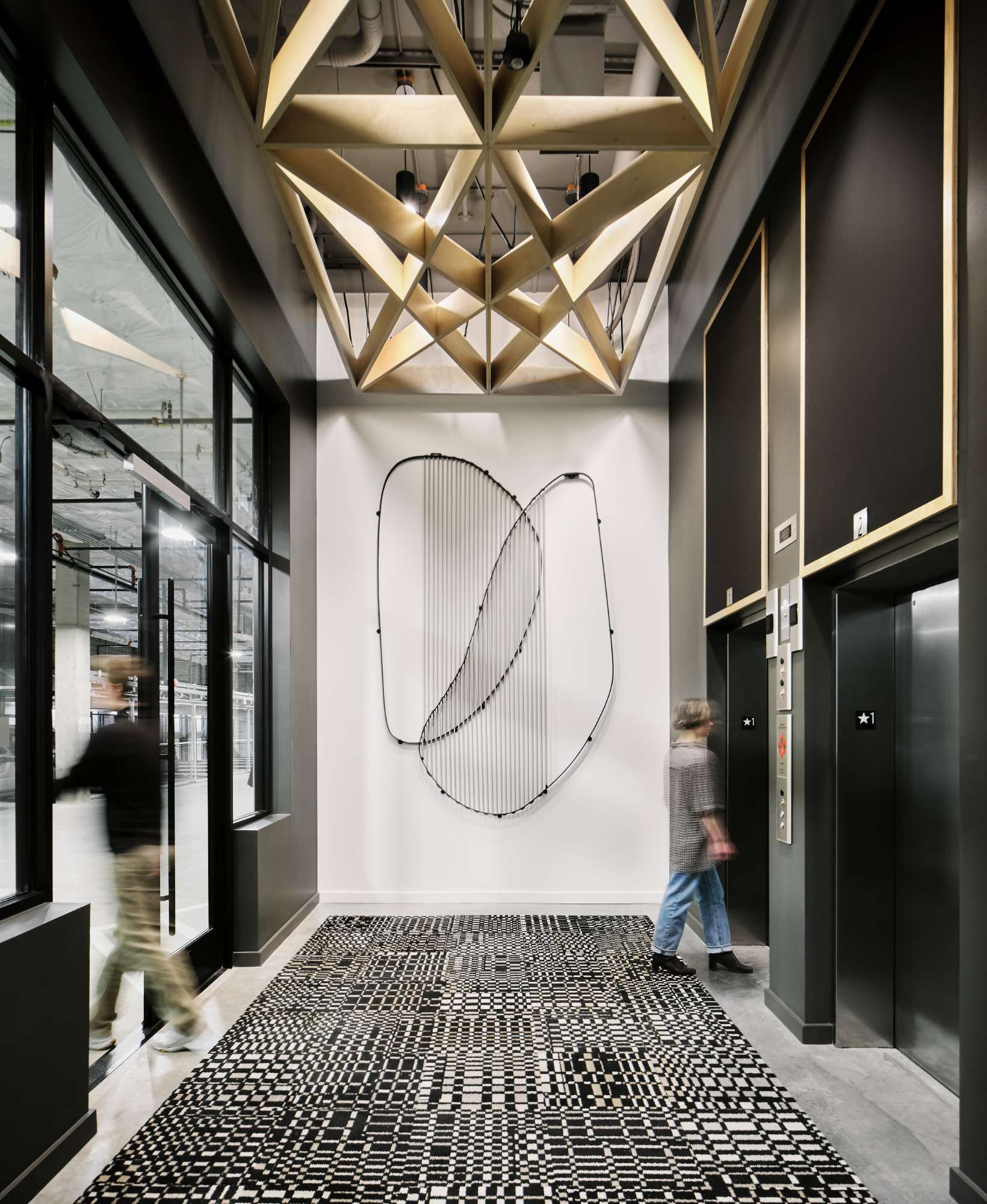 550 MLK in Portland, OR features a modern building lobby with advanced lighting and electrical solutions, supporting two elevators, dynamic lobby lighting for a geometric patterned floor and wooden lattice ceiling, and power for a large metal wall sculpture. Reliable electrician services ensure the smooth operation and maintenance of all electrical systems in this high-traffic space.