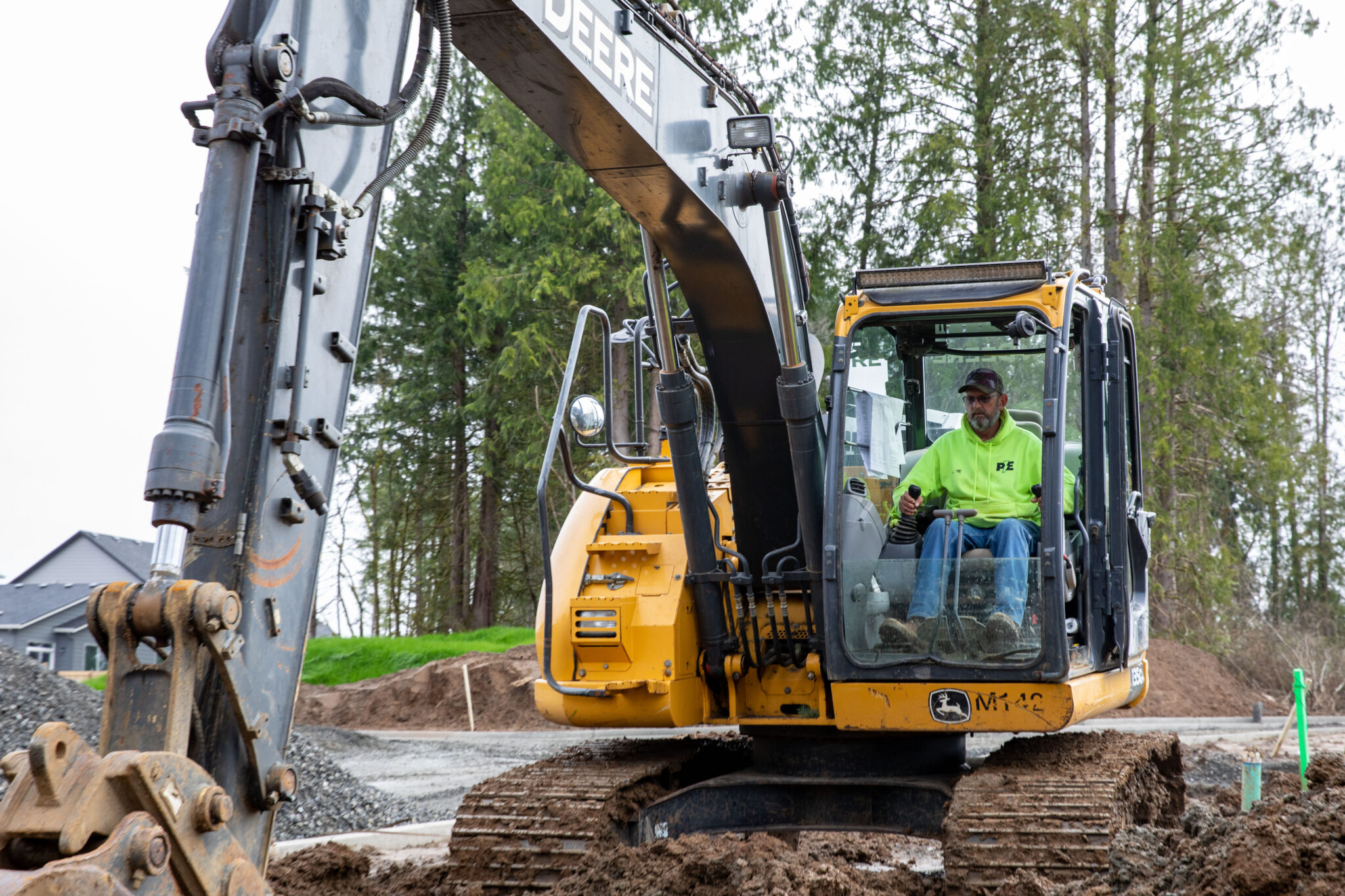 An electrician in Vancouver, WA, operates a yellow excavator at a construction site, expertly preparing the earth for electrical infrastructure.