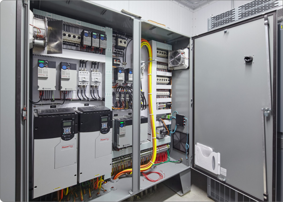 An open electrical control panel with various integrated wiring, circuit breakers, and two PowerFlex drives showcases the interior components used for industrial automation and control, illustrating the meticulous work of a skilled electrician.