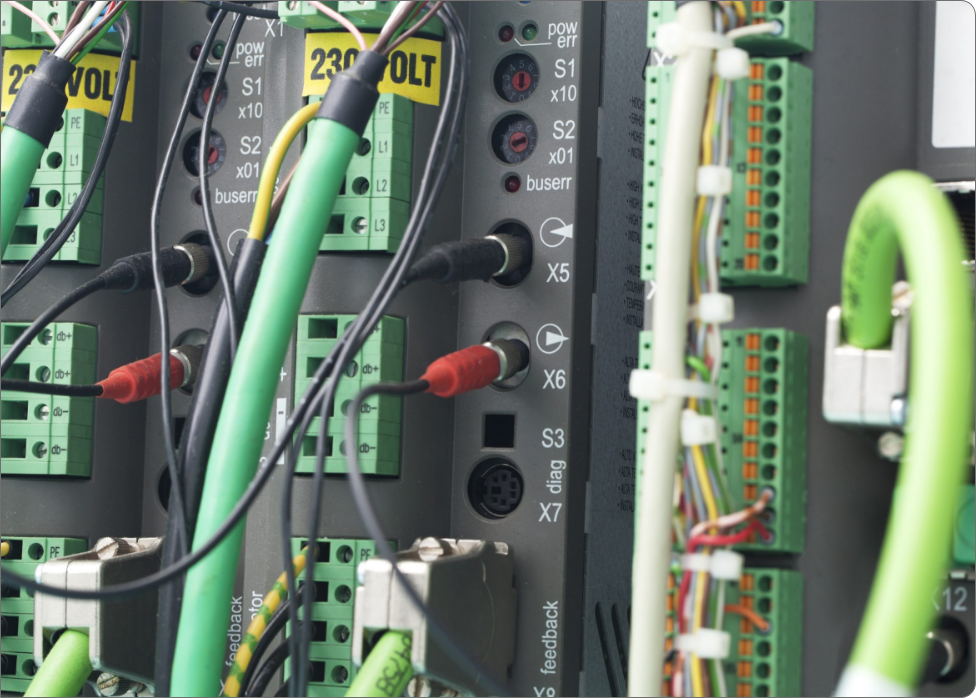 Close-up of a network switch panel with various green and black cables connected, handled meticulously by a Vancouver electrician. Yellow "230 Volt" labels are visible above some ports, ensuring electrical safety. Multi-colored wires are also seen on the right side.