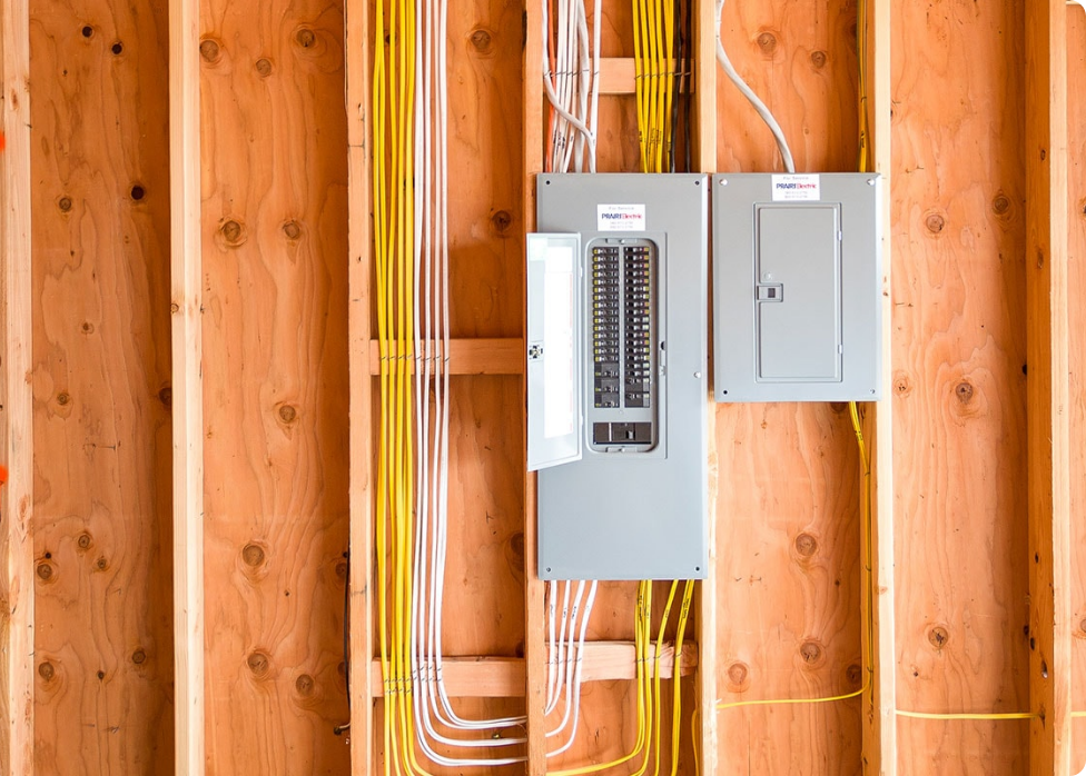 An exposed electrical panel with multiple yellow wires is seen inside the wall framing of an unfinished construction project. Several circuit breakers are visible, with one panel door open, awaiting attention from a skilled electrician in Vancouver, WA.