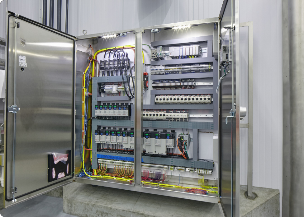 Open electrical panel with various circuits, wires, and components neatly organized inside a metal cabinet, mounted on a concrete platform within an industrial setting, carefully installed by an experienced electrician in Vancouver WA.
