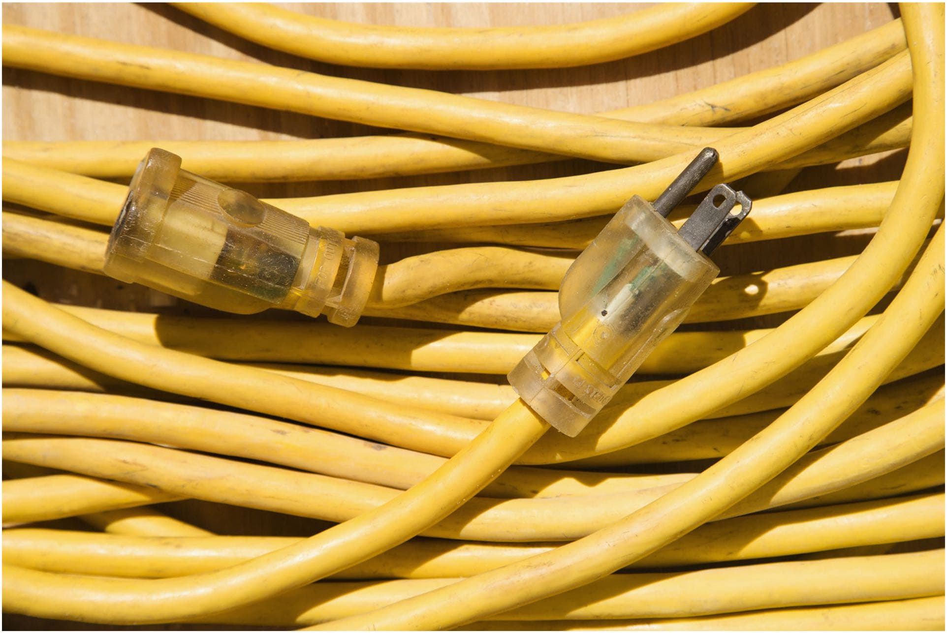 A coiled yellow extension cord with a clear plastic plug and socket lies on a wooden surface, ready for any electrical task an electrician might need in Vancouver, WA.