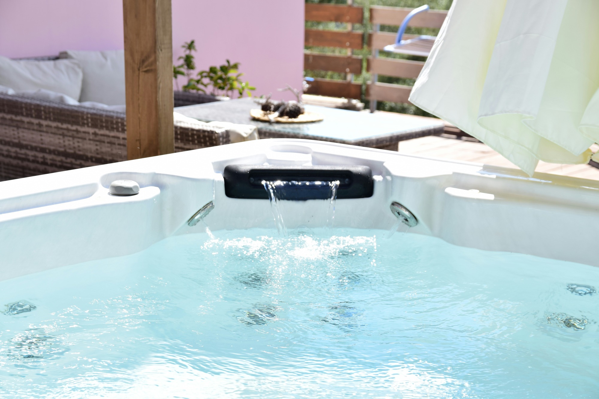 Close-up of an outdoor hot tub with water cascading from a spout, surrounded by patio furniture and plants under a sunshade—demonstrating the benefits of professional hot tub electrical installation services in Vancouver, WA.