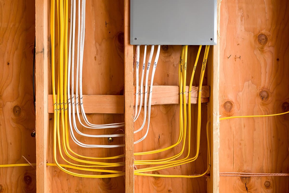 A group of yellow and white electrical wires run through the wooden framing of a wall, connected to a gray electrical box, skillfully installed by an electrician in Vancouver WA.