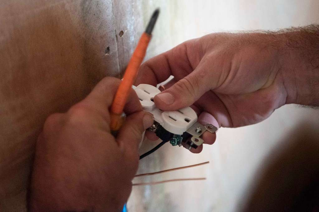 Hands meticulously replacing an electrical outlet with the help of a screwdriver.
