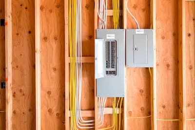 An open electrical panel with visible wires is mounted on an unfinished wooden wall next to a closed electrical box, ready for a Vancouver electrician to ensure everything is up to code.