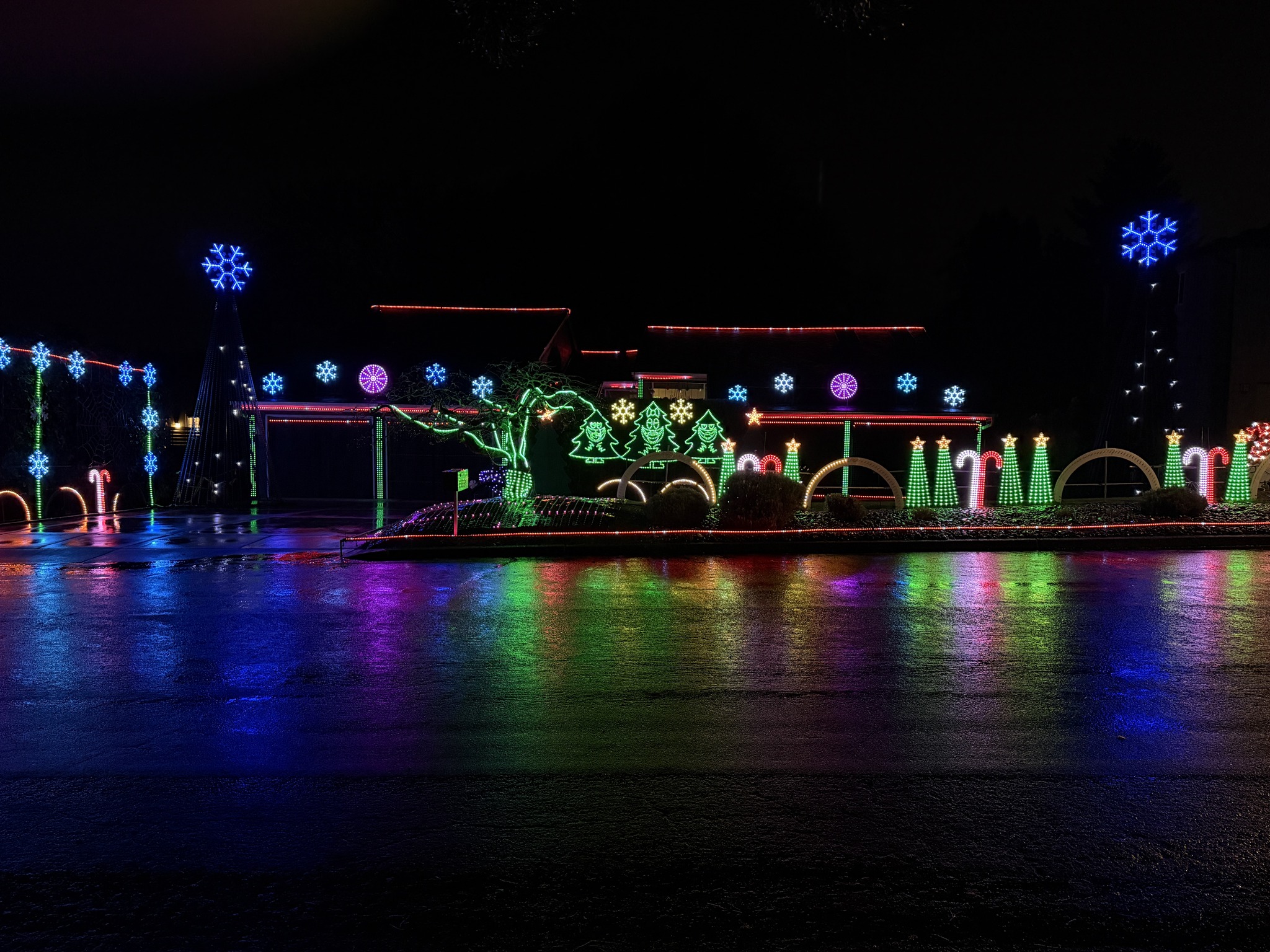 Colorful Christmas lights professionally installed on a Vancouver, WA home and yard, glowing at night on wet pavement.
