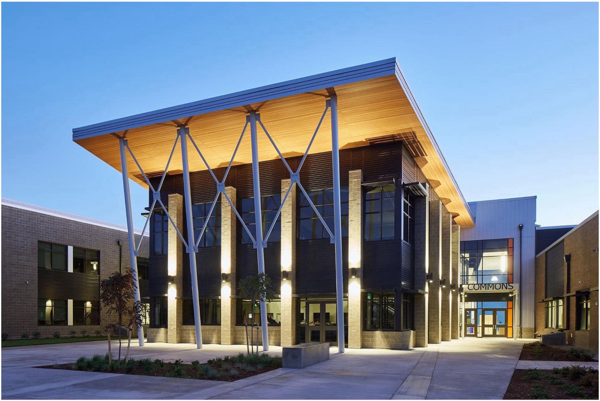 A modern two-story building with large windows, a wooden overhang, and tall support columns. The entrance is lit by the skilled work of a Vancouver electrician and marked "Commons.