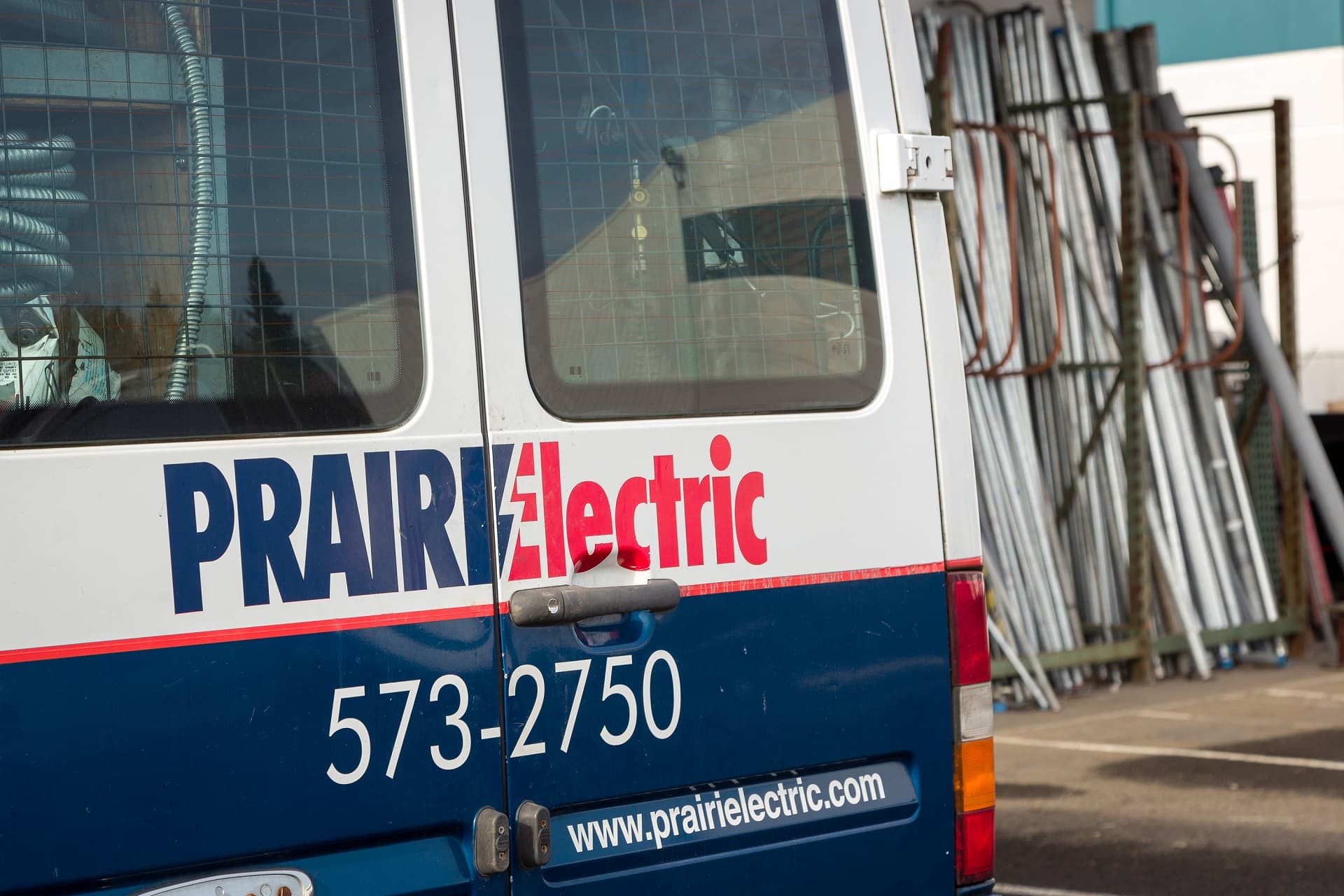 A van labeled "Prairie Electric" with the phone number 573-2750 and website www.prairielectric.com is parked near a stack of metal pipes, ready to serve as your go-to electrician in Vancouver, WA.