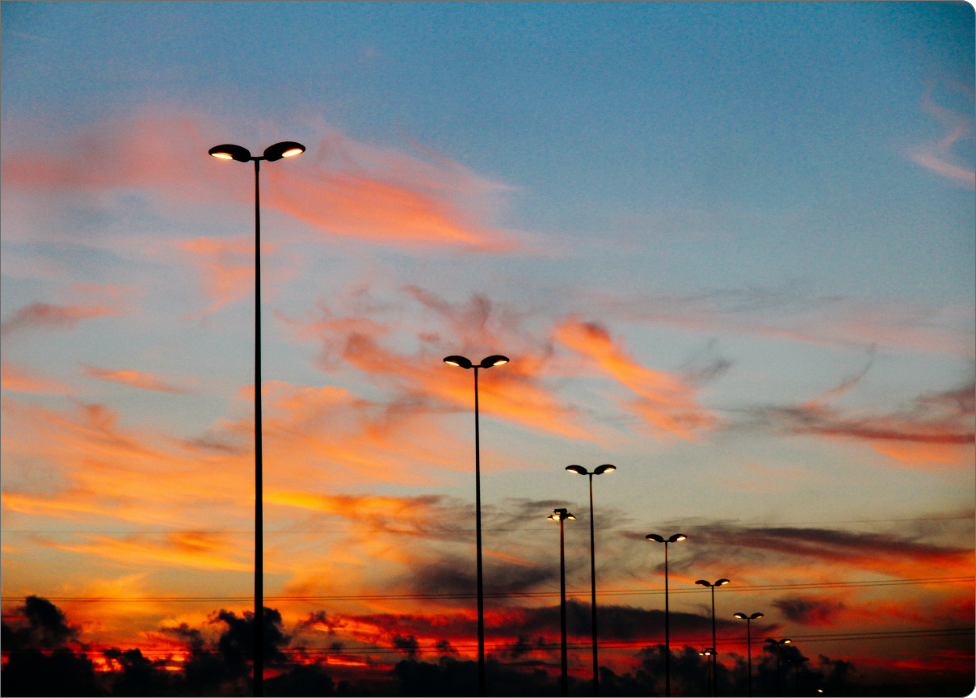 A row of streetlights illuminated against a colorful sunset sky with orange, pink, and blue hues, silhouetted against some scattered clouds—an electrician in Vancouver, WA would appreciate this picturesque twilight scene.